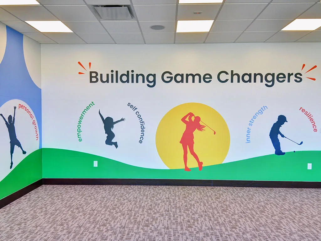 Ben Hogan Learning Center 'Building Game Changers' wall featuring silhouettes of a girl golfer, a kid jumping, and a male putter, paired with the First Tee values: personal growth, empowerment, self confidence, inner strength, and resilience