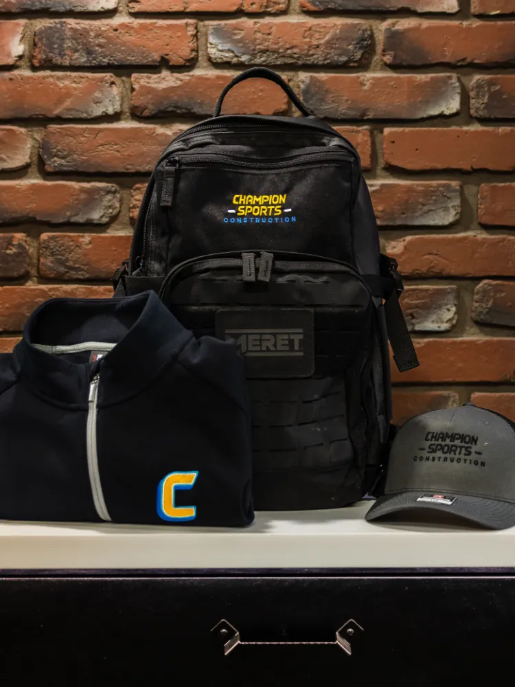 Champion Sports Construction embroidery mockups: a black backpack, navy jacket with the C patch, and a gray cap with the embroidered wordmark