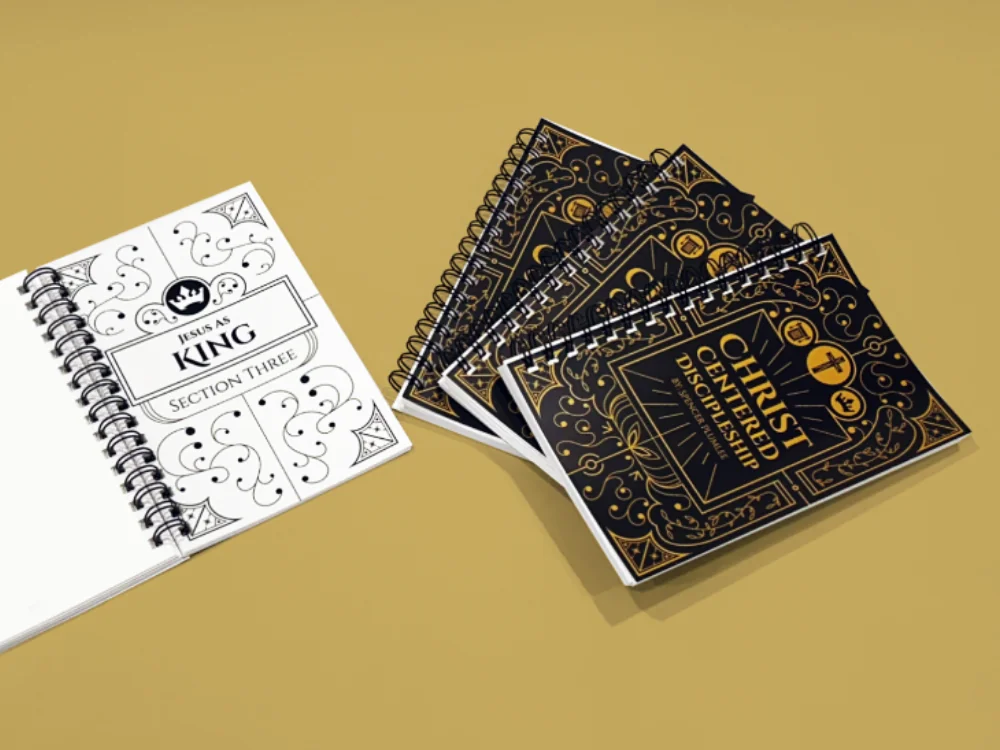Christ Centered Discipleship spiral-bound workbooks fanned out, with one open to the 'Jesus as King Section Three' page