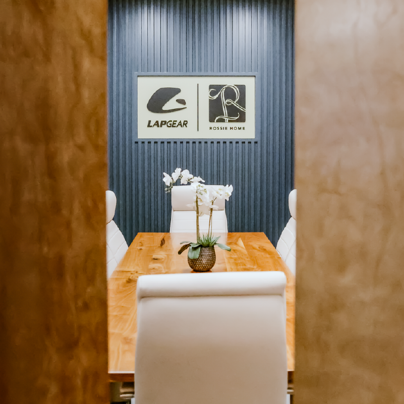Conference room console with the Lapgear and Rossie Home child logos framed in painted wood, alongside a small plant and framed cowboy portrait