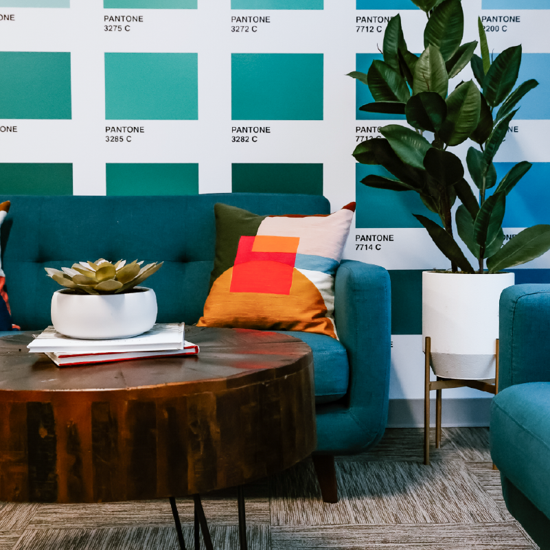 Pantone color swatches in teal, aqua, and blue covering a feature wall behind a teal velvet sofa with patterned throw pillows