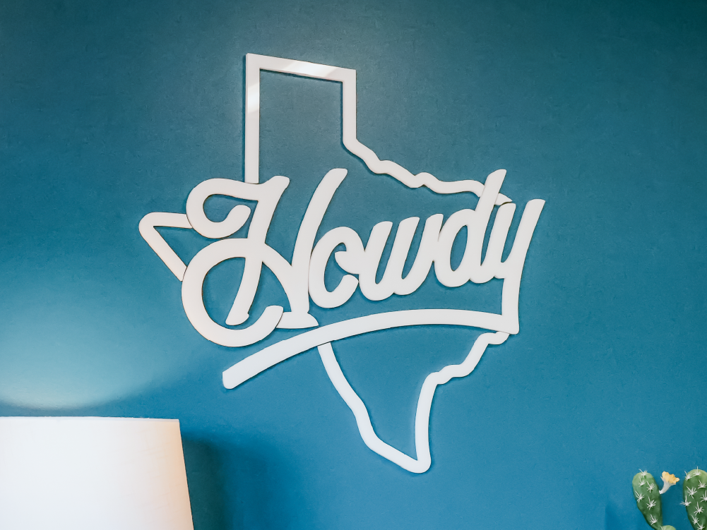 Texas-shaped 'Howdy' script sign mounted on a teal painted accent wall