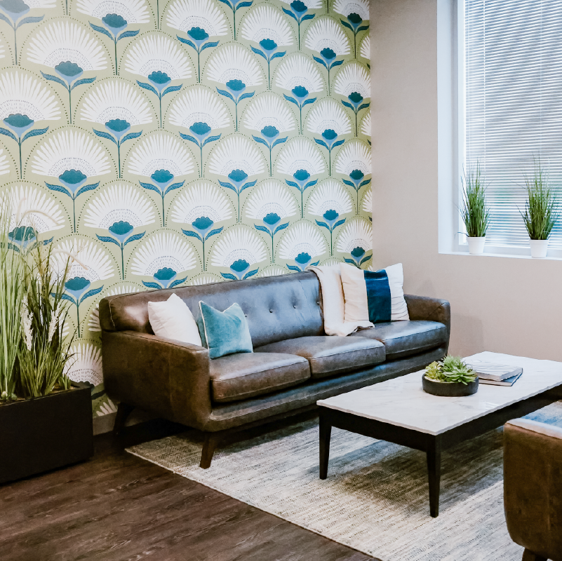 Creative Manufacturing office lounge with magnolia bloom wallpaper, a brown leather sofa with throw pillows, and a marble-topped coffee table