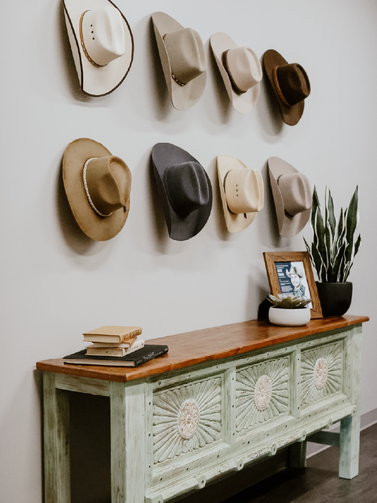 Cowboy hats arranged on a wall above a green painted console table styled with stacked books and a framed cowboy portrait