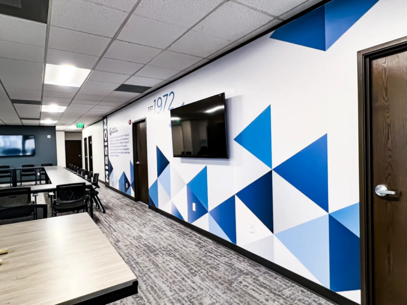 Graham Associates conference room corridor with a large-scale triangle pattern wall, a mounted television, and the EST. 1972 typographic feature