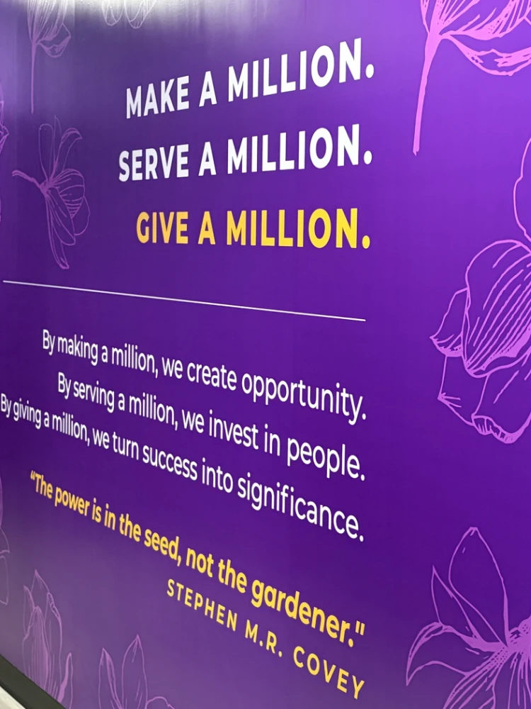 Custom vinyl wall reading 'Make a Million. Serve a Million. Give a Million.' with a Stephen M.R. Covey quote on a deep purple wall with magnolia bloom illustrations