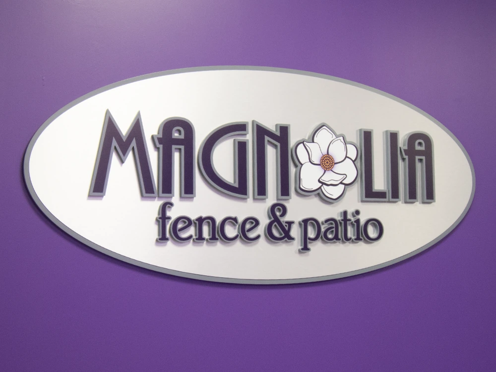 Magnolia Fence & Patio reception area with a custom dimensional oval logo plaque, magnolia bloom wallpaper, and a custom purple reception desk with a natural wood top and purple resin inlay