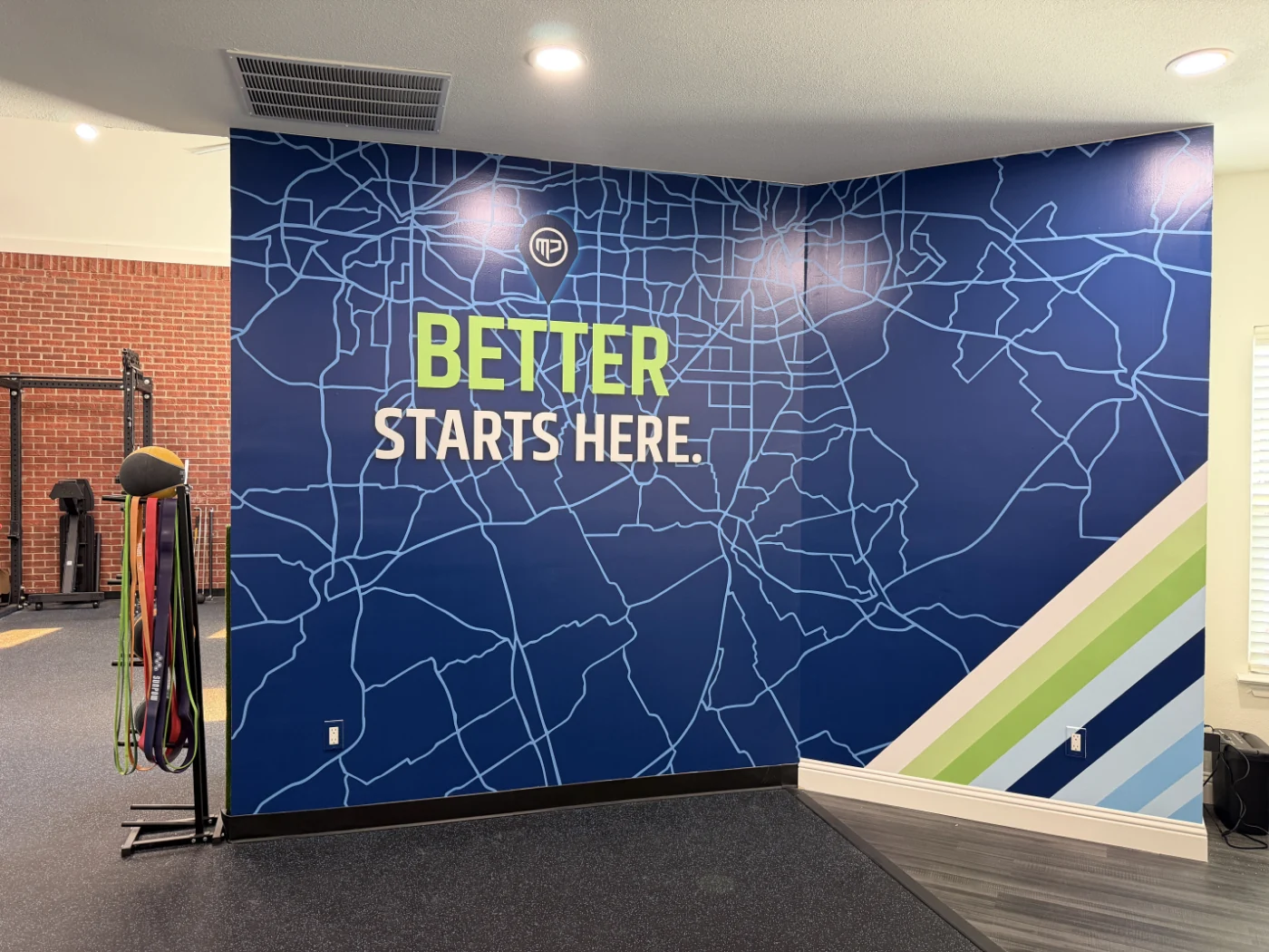 Custom vinyl wall featuring a stylized Dallas-Fort Worth road map with the MyPhysio location pin and the phrase 'Better Starts Here.' inside the studio gym