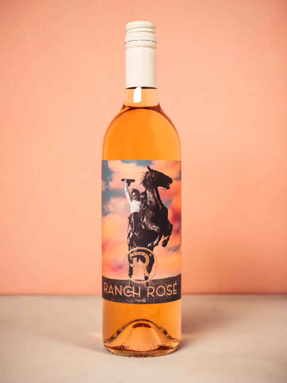 Ranch Rosé bottle close-up on a peach background featuring the rearing horse and cowboy label on a sunset sky