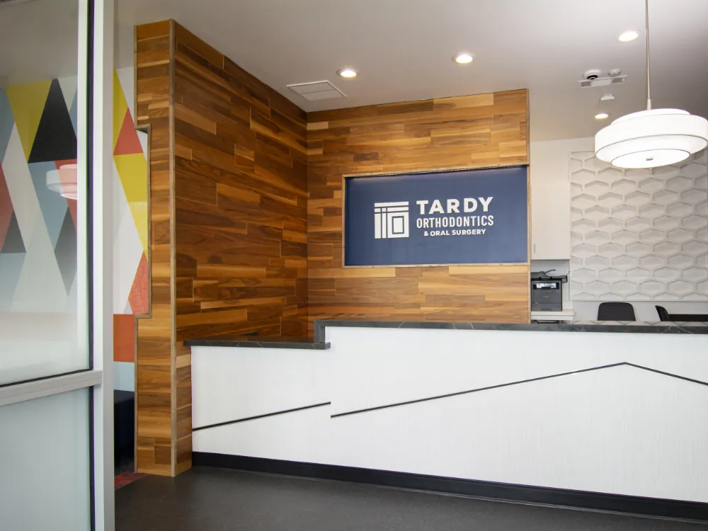 Tardy Orthodontics & Oral Surgery North Richland Hills office reception with a wood-paneled accent wall, dimensional brand sign on a navy panel, and a white reception desk