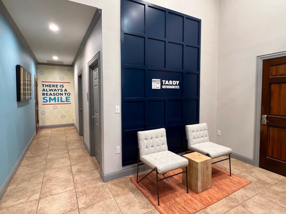 Tardy Orthodontics interior feature wall with a dimensional logo on a navy paneled accent wall, two upholstered chairs, and the 'There Is Always a Reason to Smile' graphic visible down the hallway